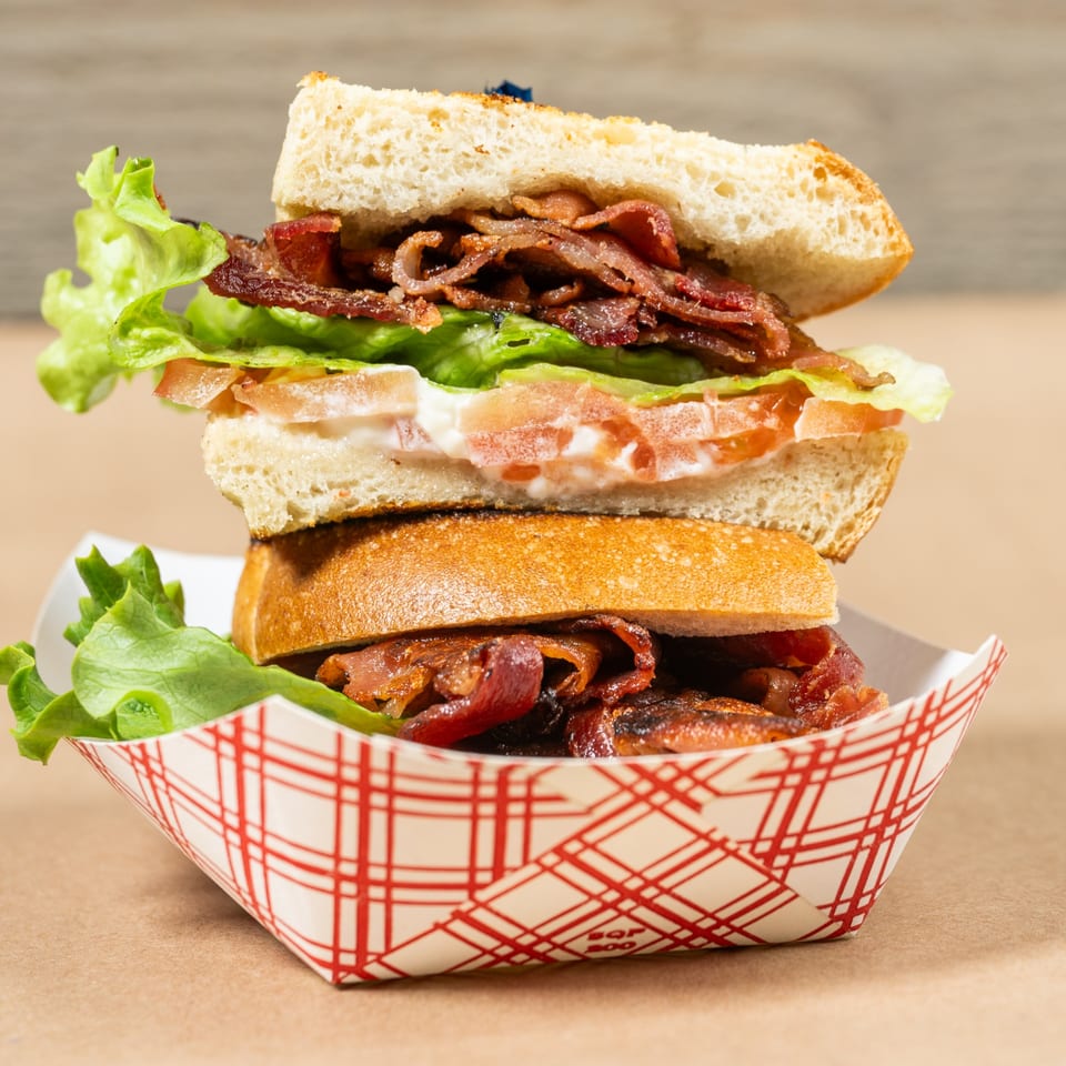 A Squeeze Burger BLT sandwich with bacon, lettuce, tomato, and mayo in a red-checkered paper tray.