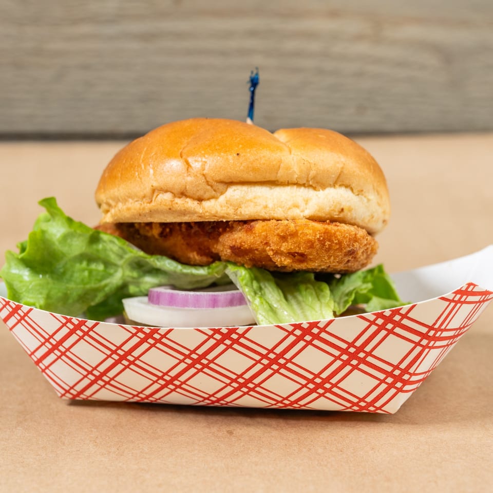 Squeeze Burger's crispy chicken sandwich with lettuce and red onion in a red and white checkered tray.