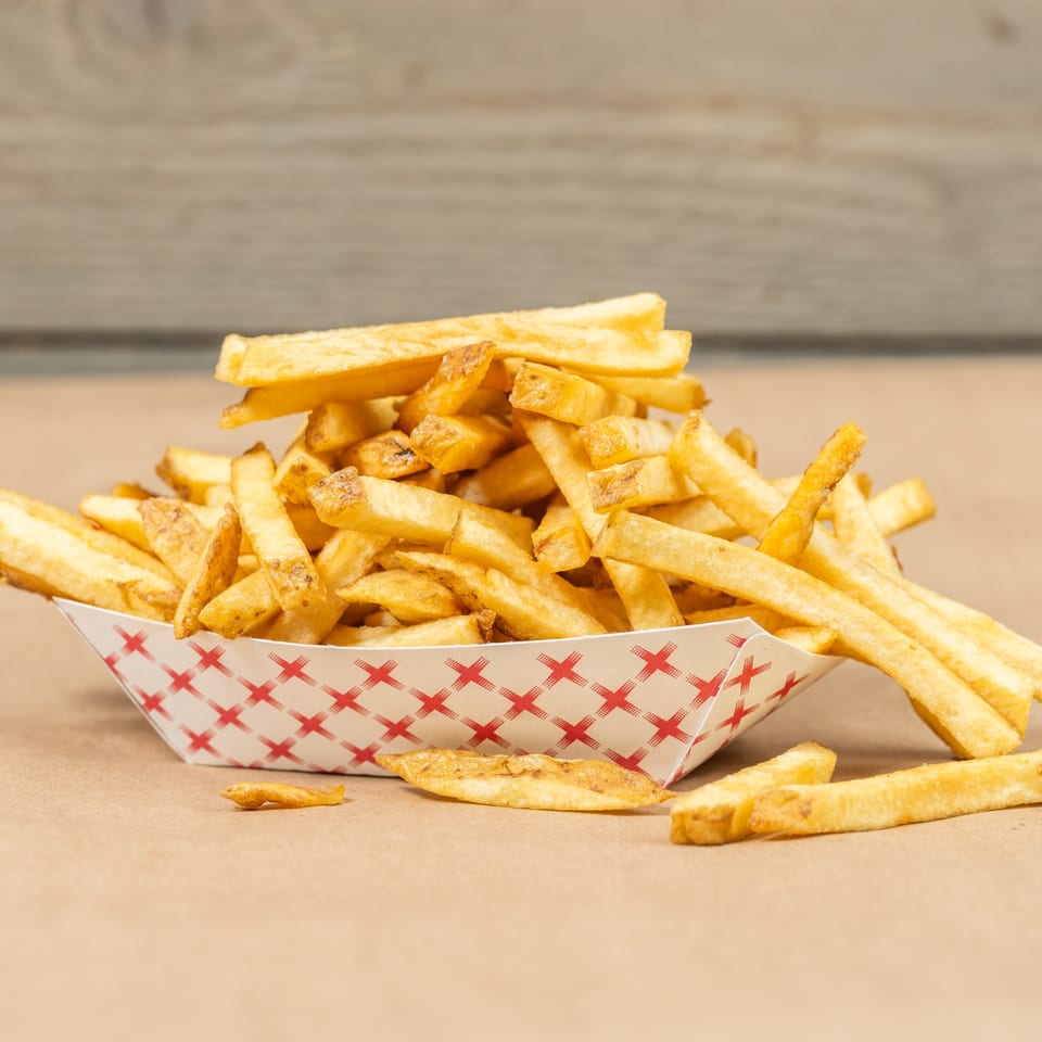 A paper boat filled with golden-brown Squeeze Burger fries, with some scattered on a brown surface.