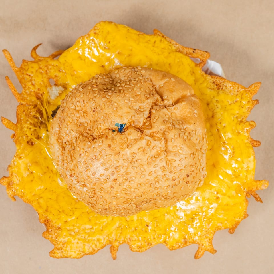 Top-down view of a Squeeze Burger with a sesame seed bun and a large skirt of melted, crispy cheese.